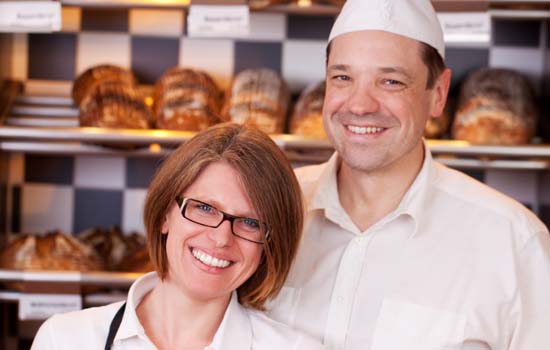 Bäckerin und Bäcker vor Verkaufsregal mit Brot und Gebäck