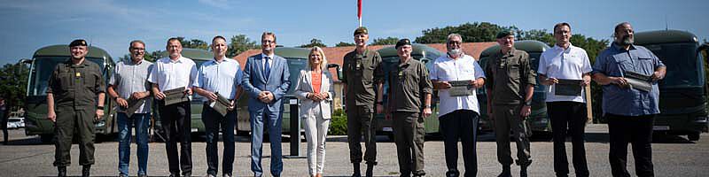 Ministerin Klaudia Tanner bei der Übergabe der neuen Reisebusse mit den zukünftigen Fahrern und BBG Geschäftsführe Gerhard Zotter. Im Hintergrund sind die Busse zu sehen.